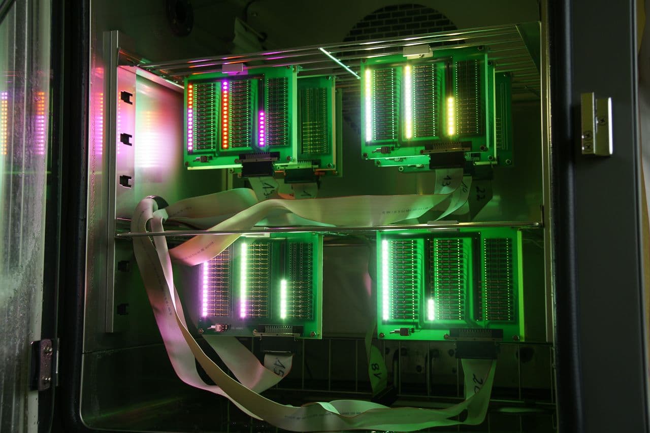 View into the climate chamber: four LED test boards lit in green, yellow and magenta, connected by ribbon cables.